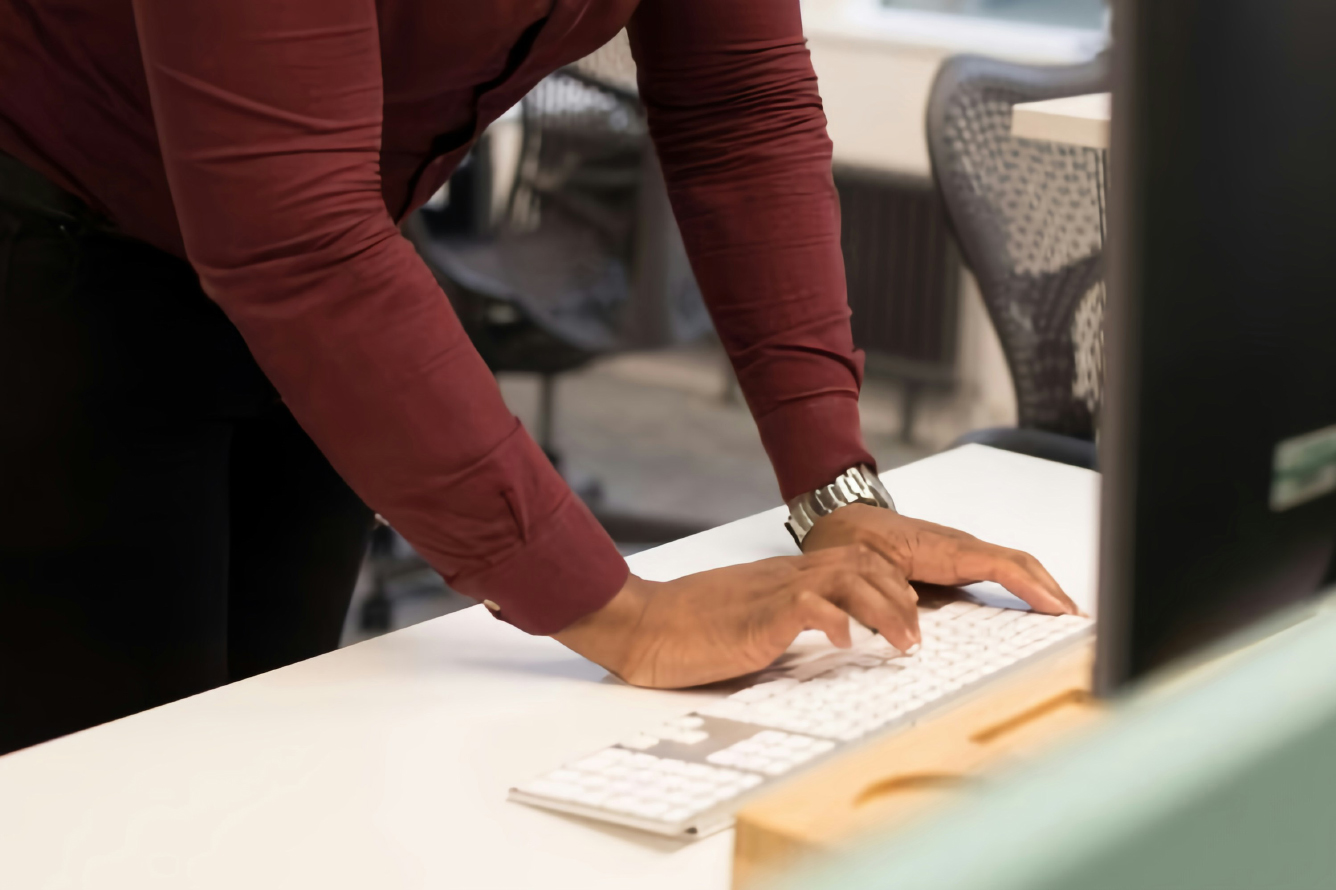 A woman stands at a desk while typing.
